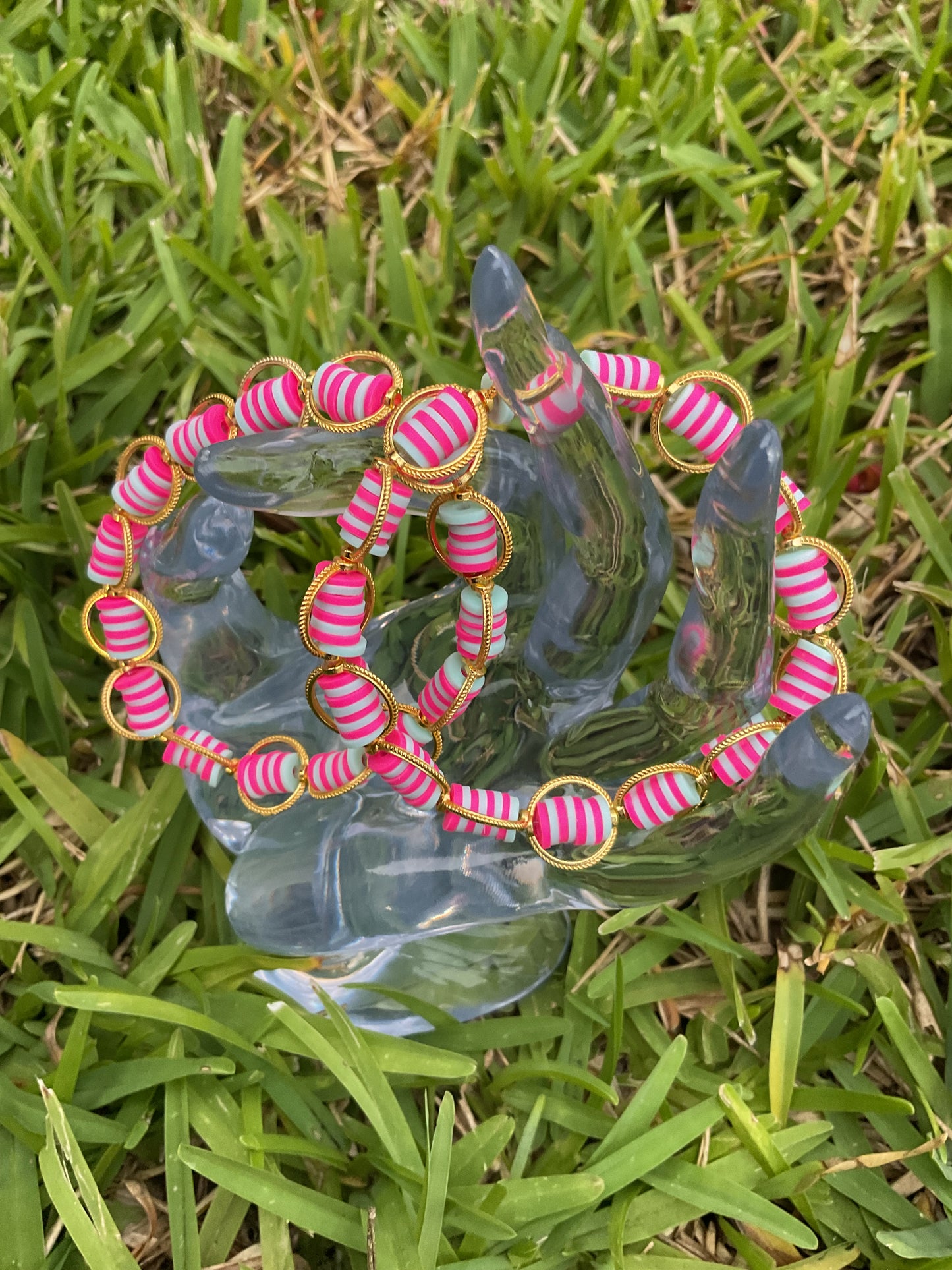 Decorative glass sculpture with pink and gold beaded chain on grass